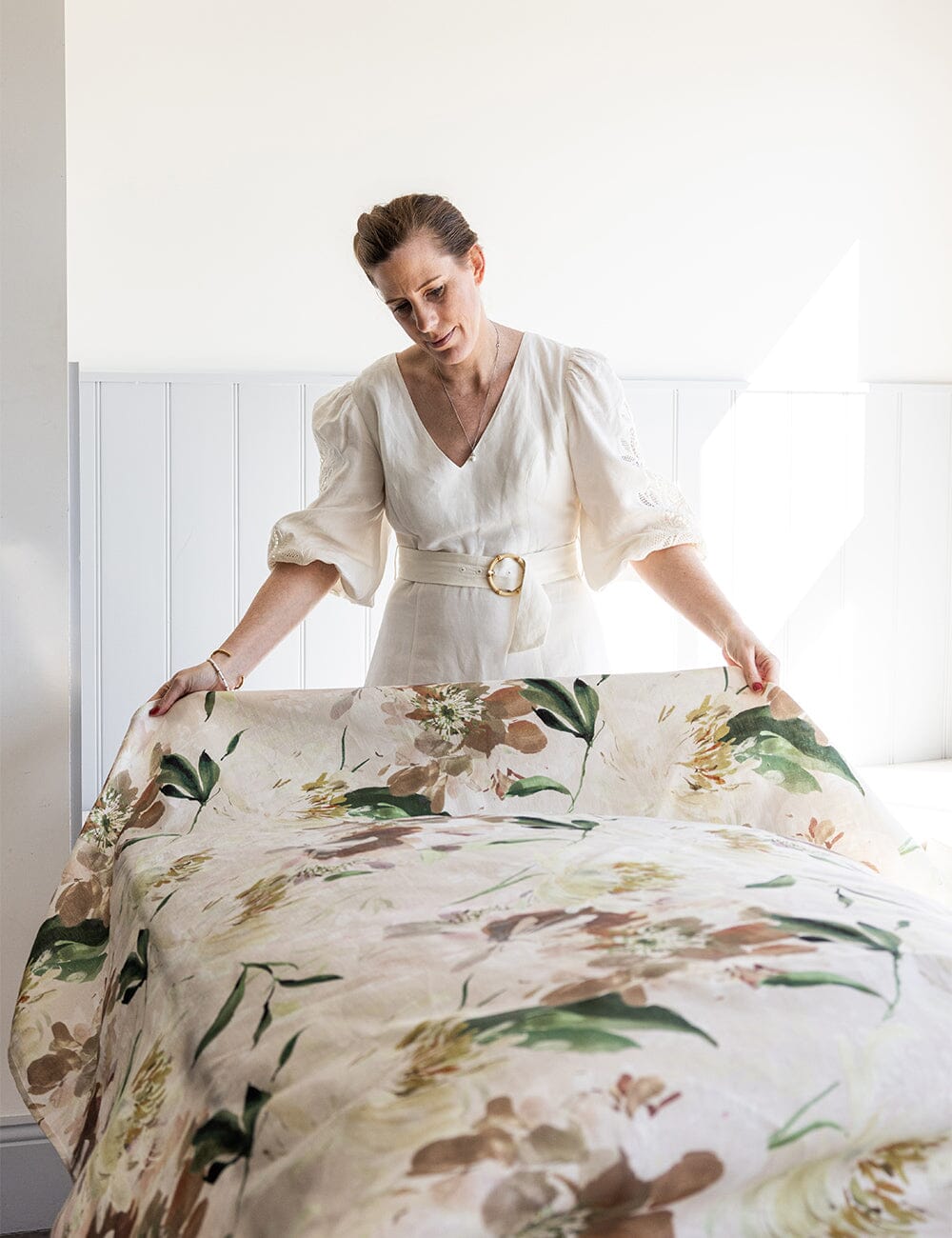 Woman setting a table with the designer Peony Study linen tablecloth, showcasing its botanical floral design in soft natural light.