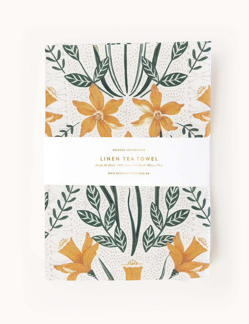 Folded Bespoke Letterpress linen tea towel featuring a hand-illustrated daffodil design in golden ochre and rich green tones, wrapped in a branded paper band.
