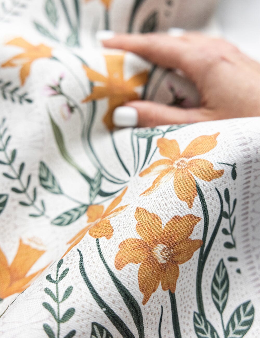 Close-up of a hand holding a softly draped Bespoke Letterpress linen tea towel, showcasing detailed golden daffodil and leafy botanical illustrations on textured natural fabric.