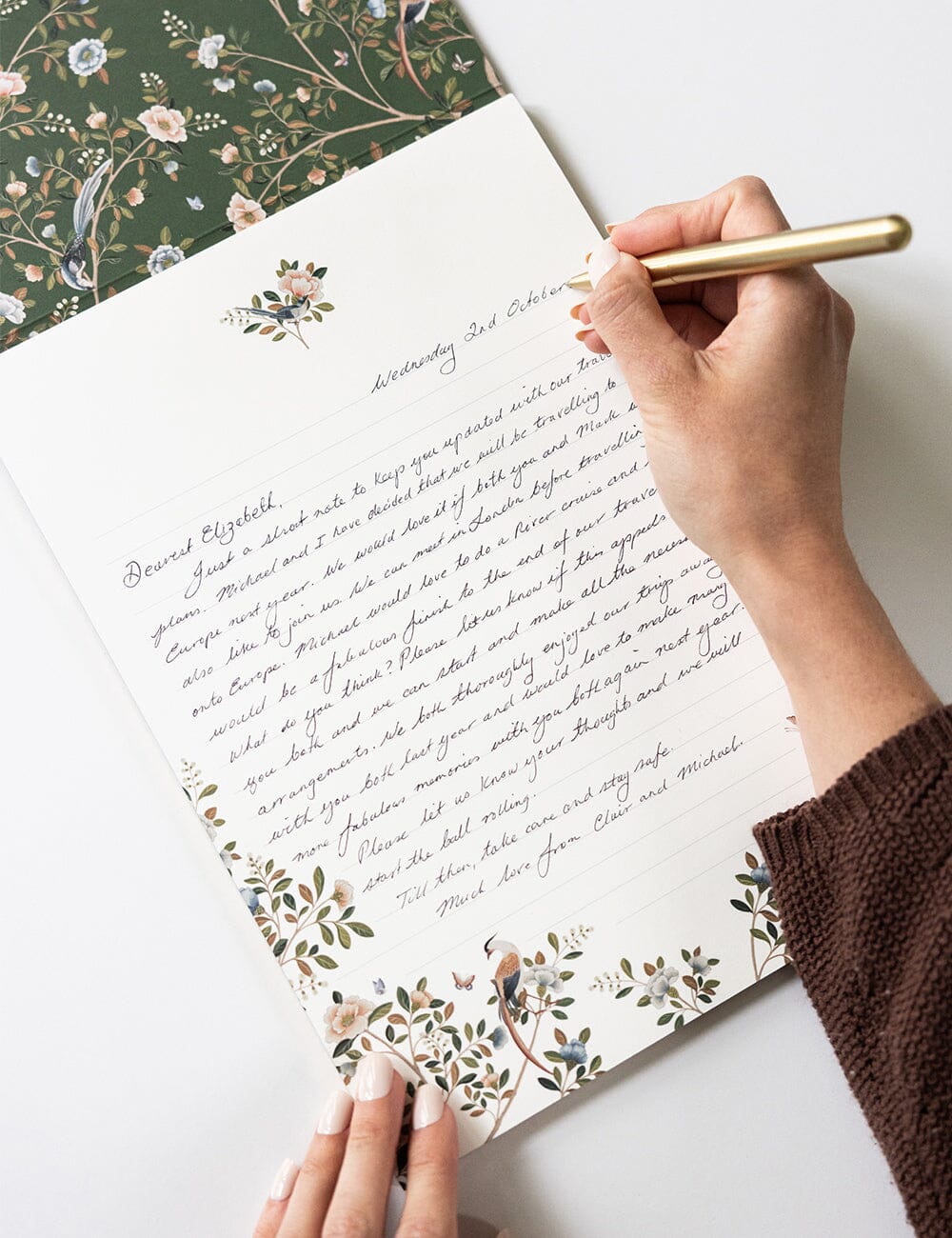 A hand holding a gold pen while writing a heartfelt letter on the Camellia Tree A4 Writing Pad, adorned with botanical borders and delicate bird motifs.